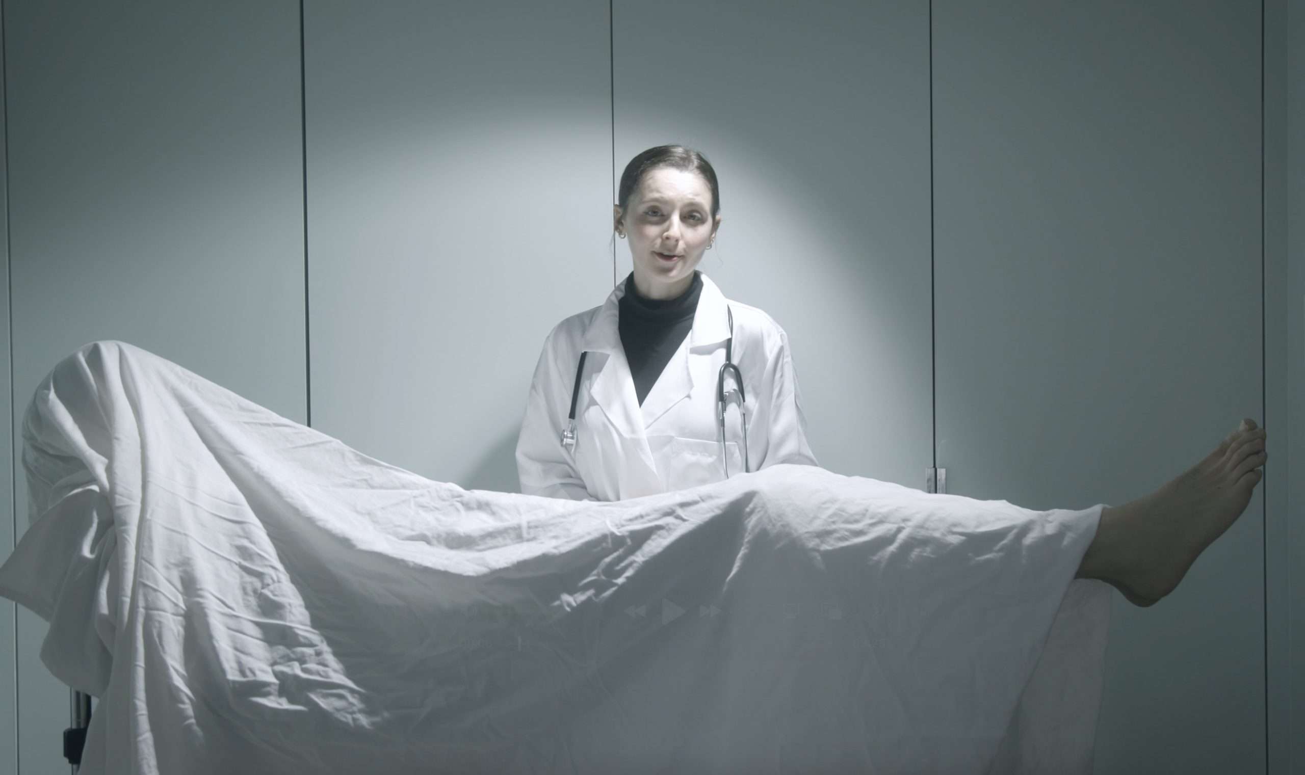Ivy Coach's enrollment coordinator, in a doctor's lab coat, stands over a body on an operating table.